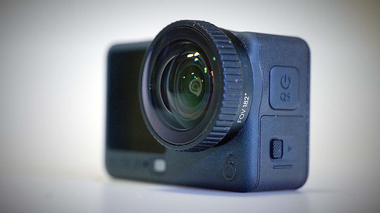 The image shows a compact action camera, the DJI Action 6, with a wide-angle lens and a rugged design. It features buttons on the side for operation, including a power button and a quick select (QS) button. The camera is designed for adventure and outdoor photography, likely capable of capturing high-quality video and images in various conditions.