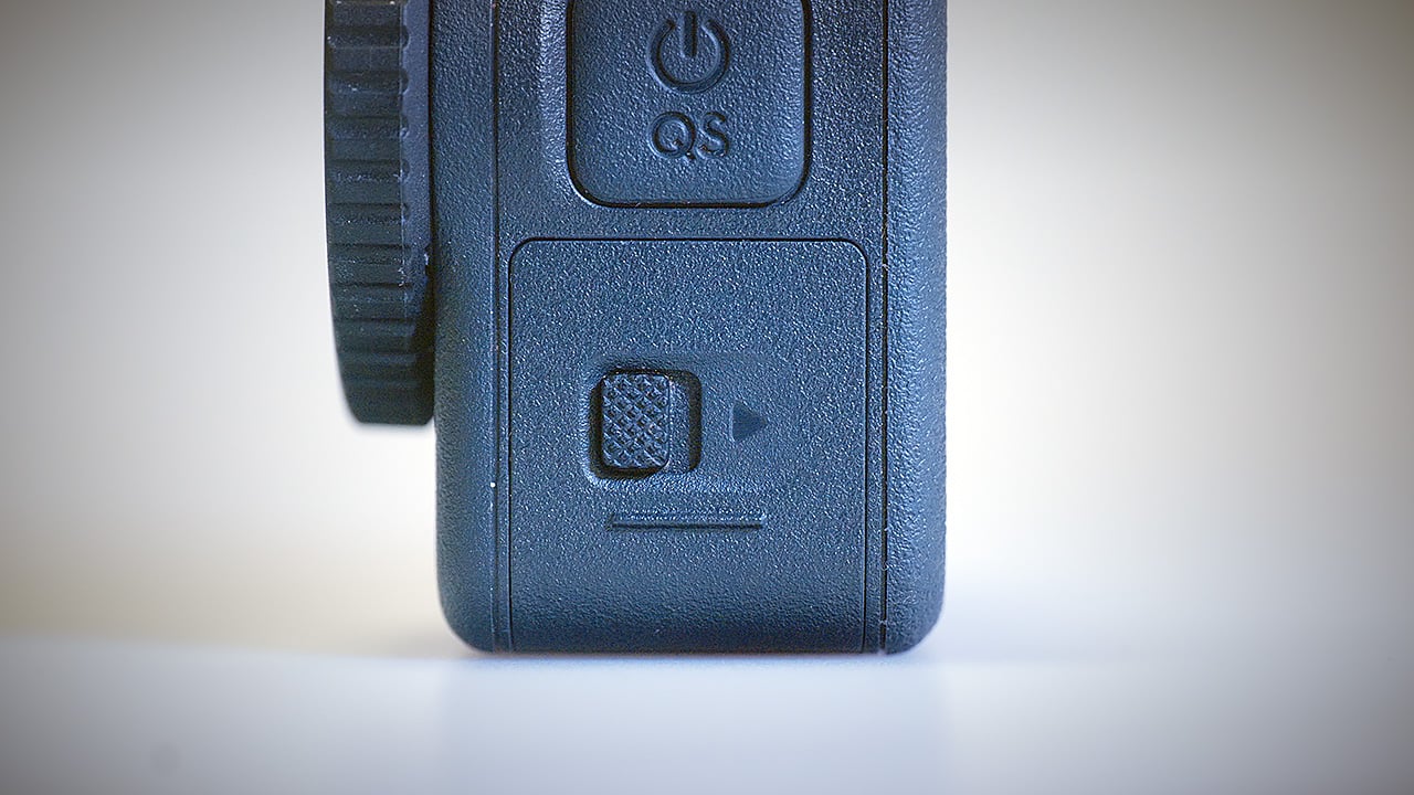 The image shows a close-up view of the DJI Action 6. It features a textured, black surface with buttons, including a power button and a playback or record button, indicated by a triangle symbol. The design suggests functionality for quick access to features, with a control dial visible on the side.
