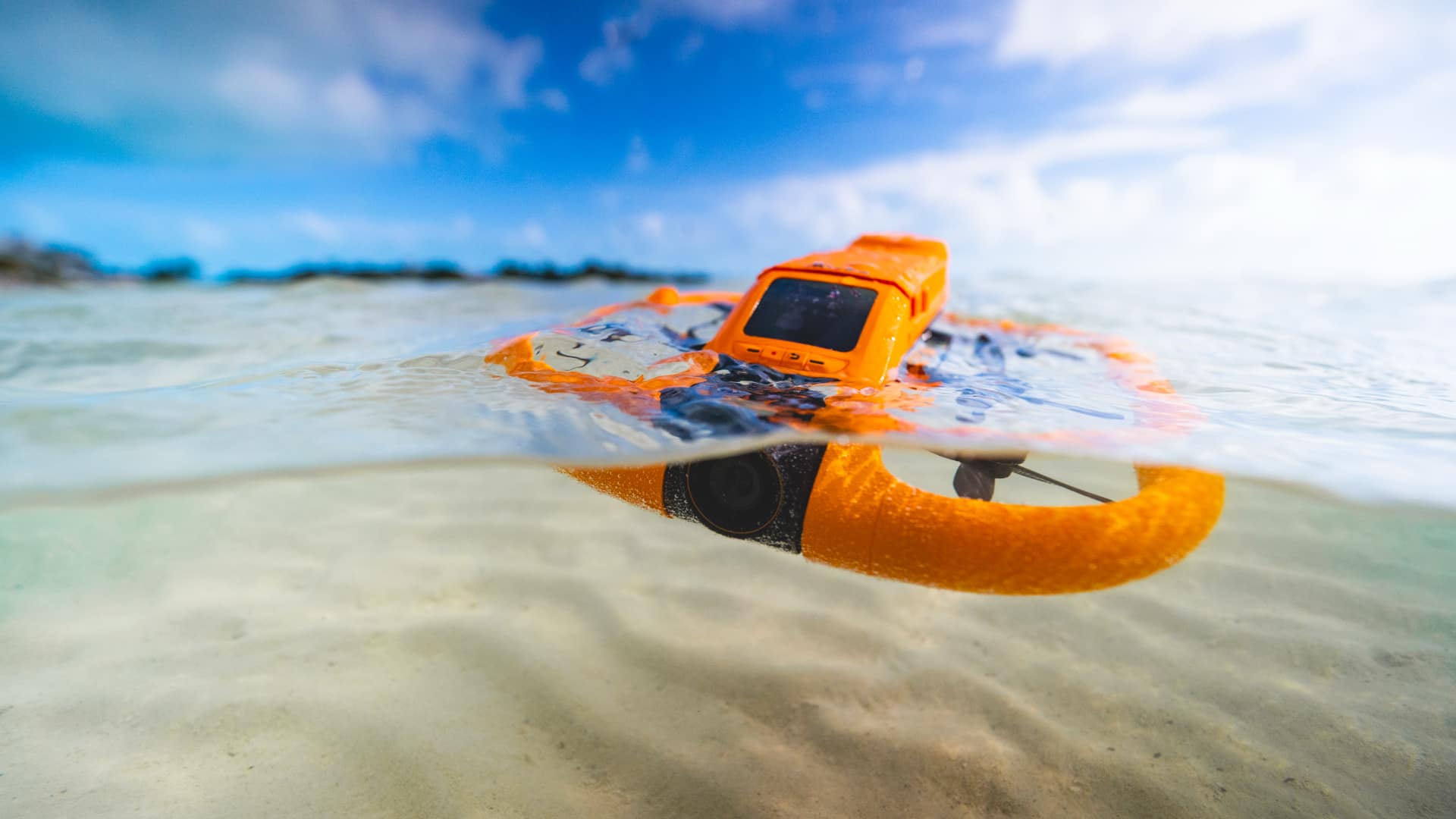 HOVERAir AQUA floating on shallow coastal water at the waterline, with sandy seabed visible beneath the surface