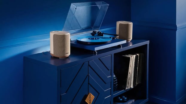 Bose Lifestyle Ultra Speaker stereo pair in Driftwood Sand finish on solid white oak bases, shown in a living room setting