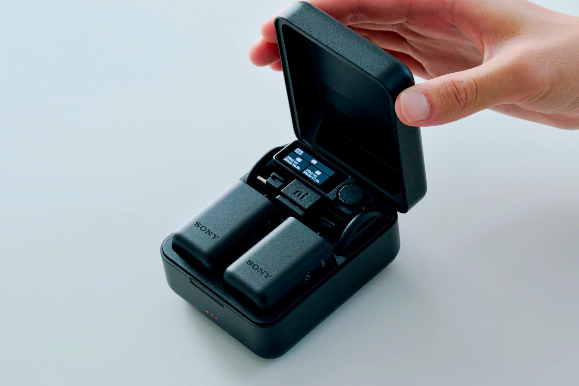 Sony ECM-W5 charging case held open by hand, with two transmitters and the receiver docked inside