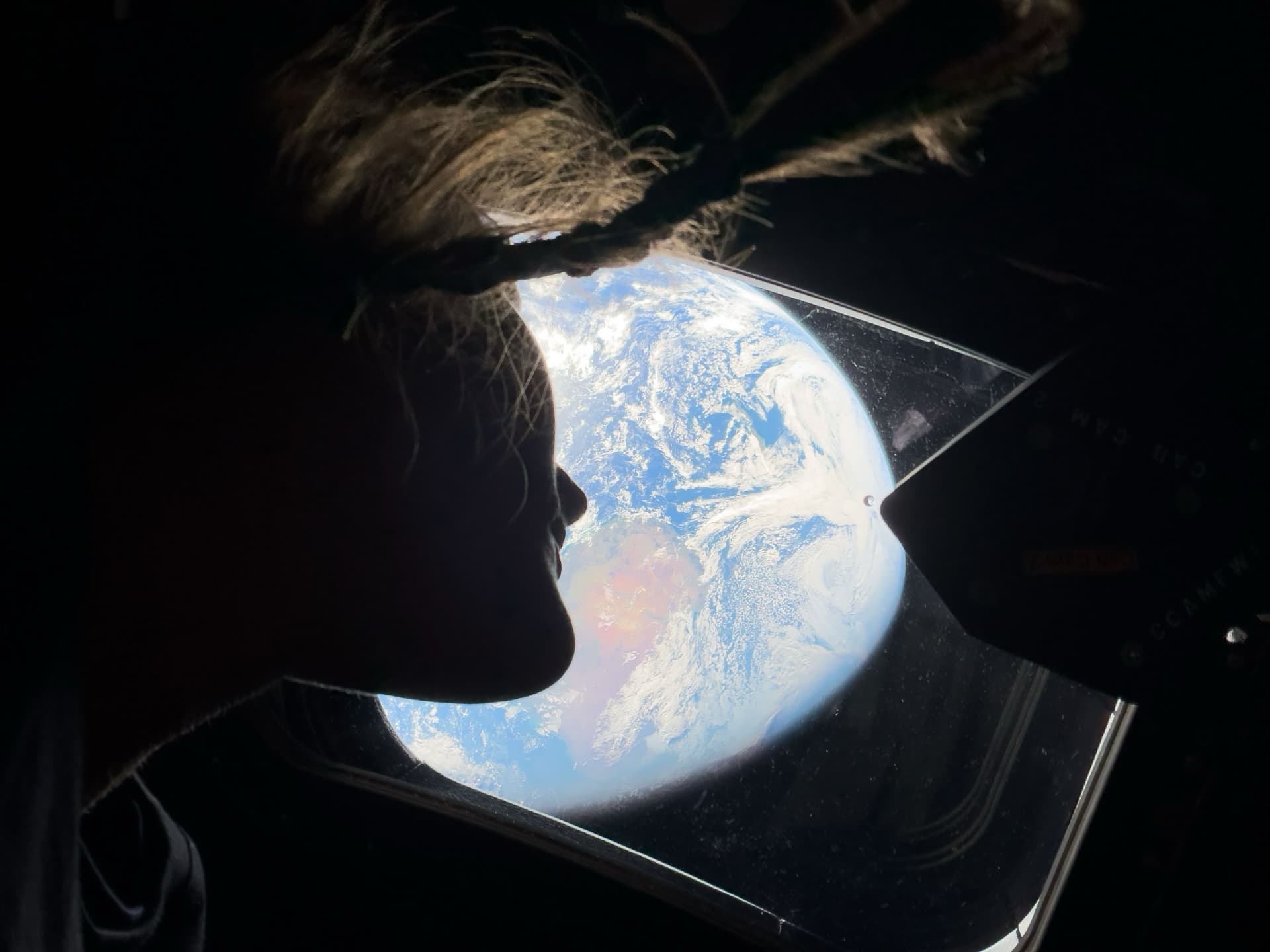 NASA astronaut and Artemis II mission specialist Christina Koch peers out of one of the Orion spacecraft's main cabin windows, looking back at Earth