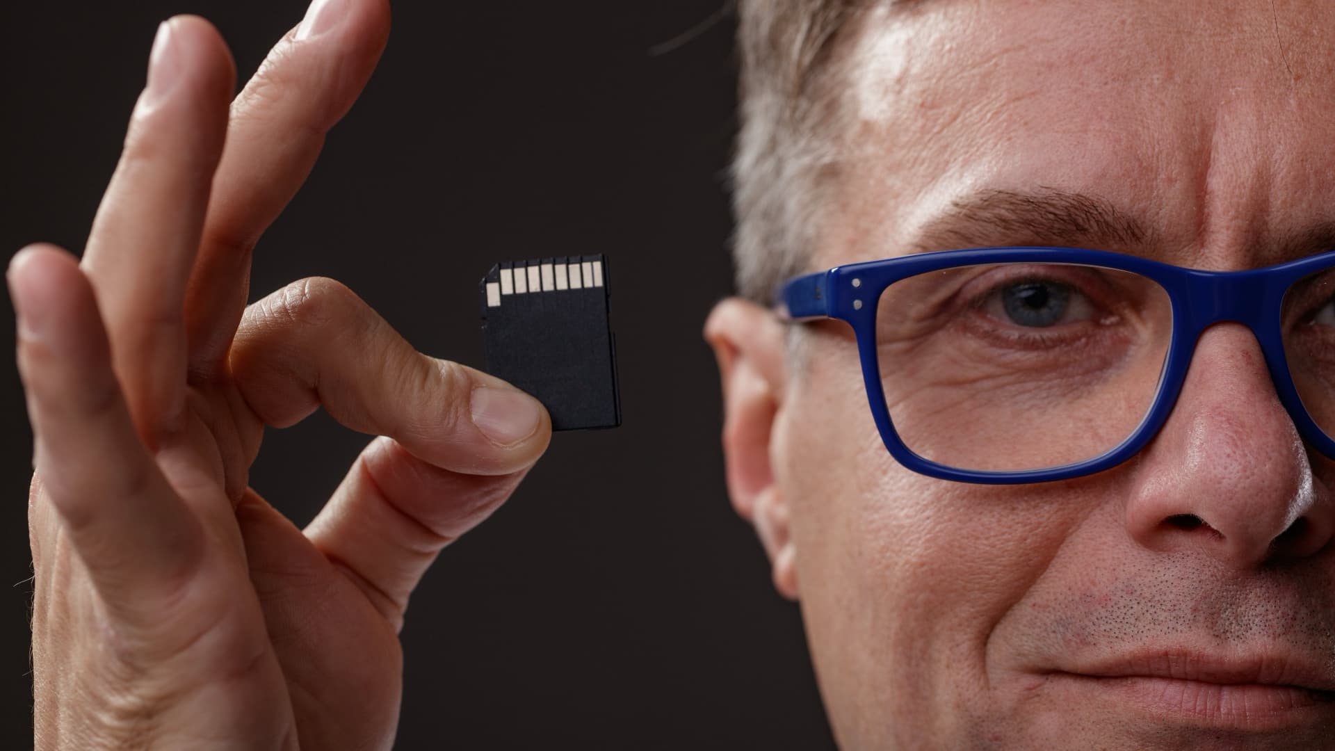Man with glasses holding a SD card up to the camera