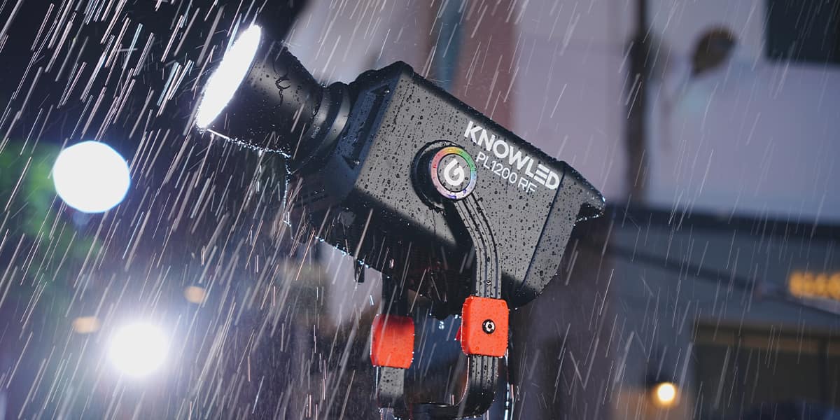 Godox KNOWLED PL1200RF fixture in use outdoors in heavy rain, showing the IP65-rated housing