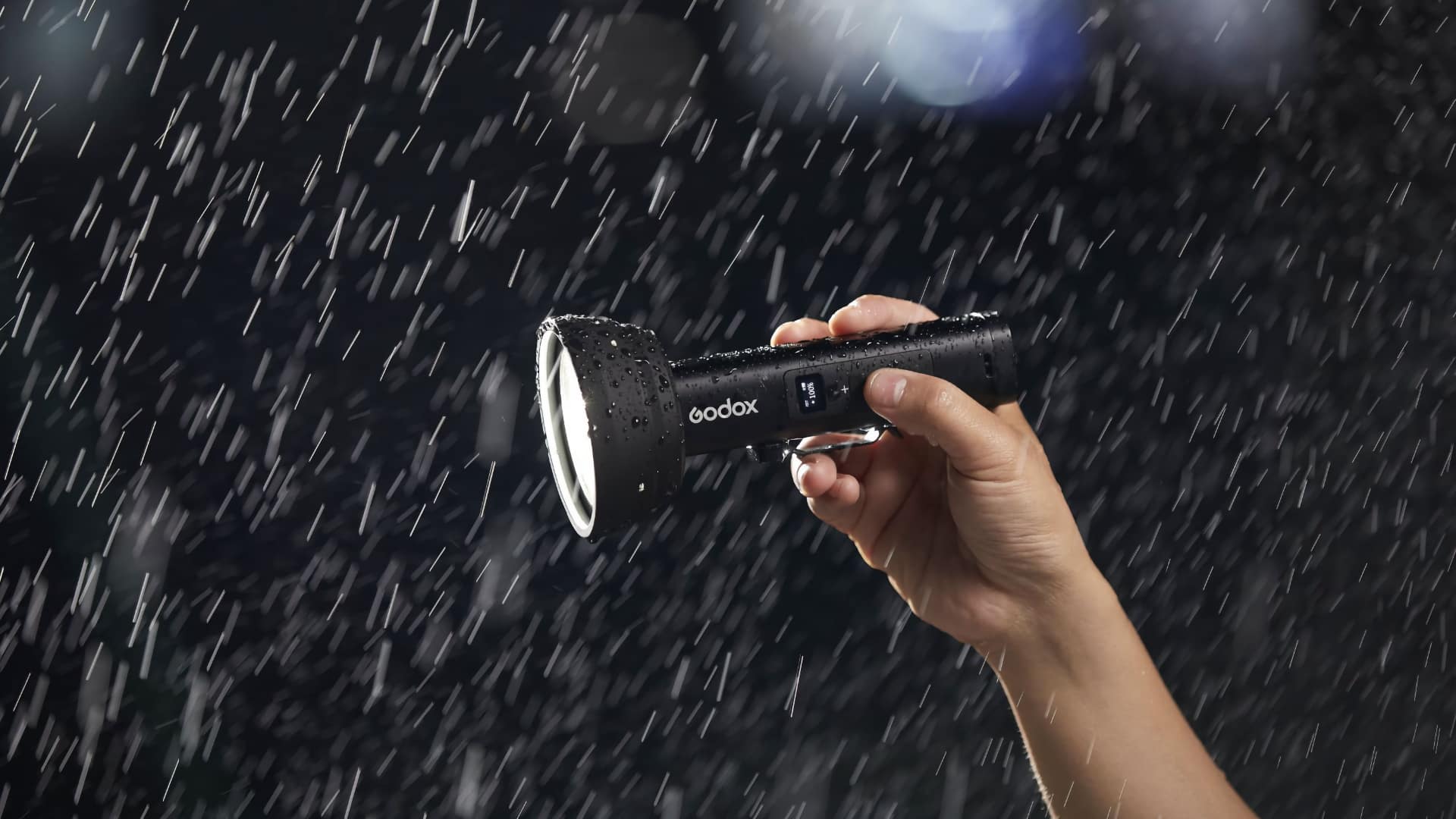 Godox FL15Bi handheld in heavy rain, demonstrating IP54 weather resistance with water droplets visible on the lens