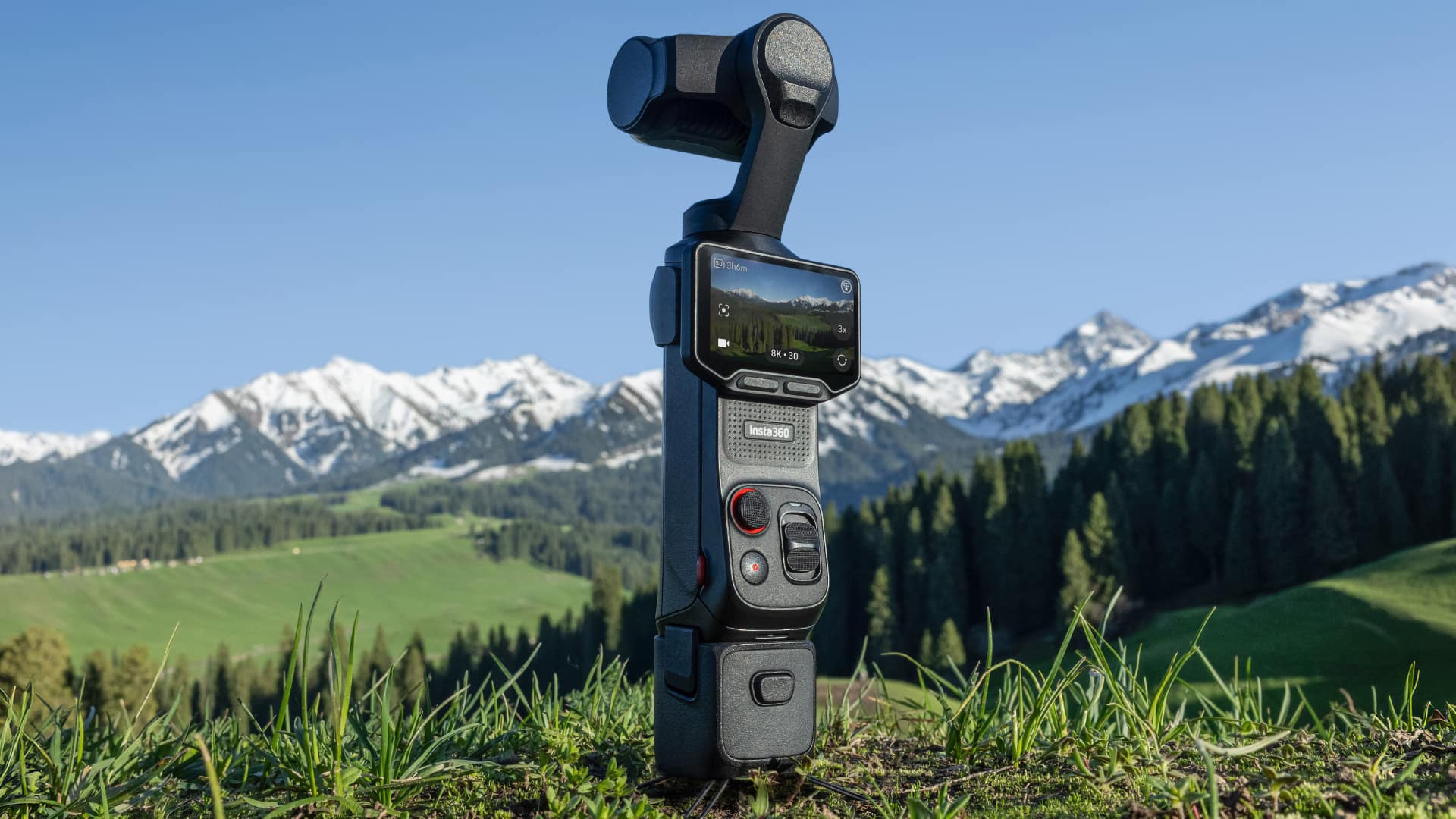 Insta360 Luna Ultra in Cosmic Black outdoors, OLED screen showing 8K30 recording at 3x zoom, alpine mountain backdrop