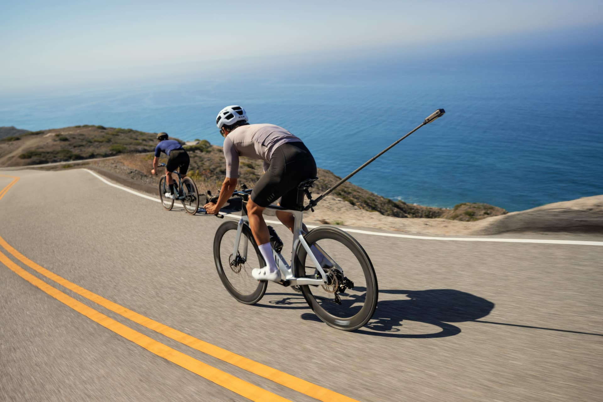 Cyclist riding a coastal road with Insta360 X6 mounted on a selfie stick pointing back over the shoulder