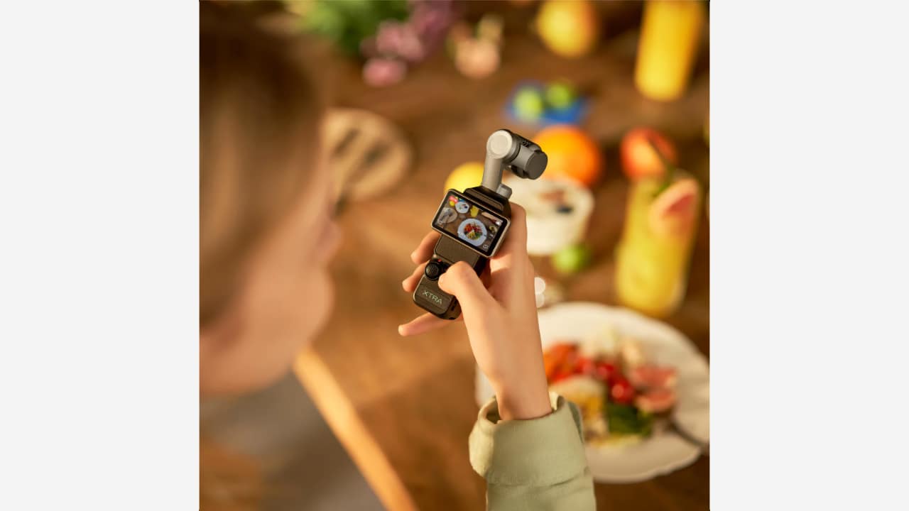 Xtra Muse 2 Pro held in hand with its flip touchscreen showing an overhead food scene